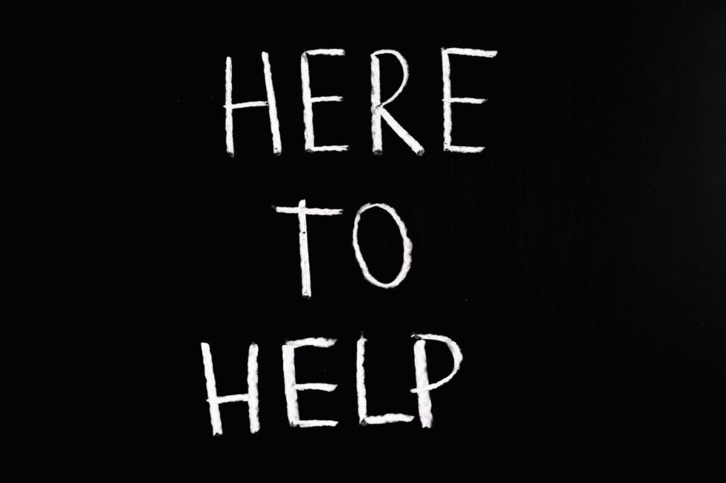 White text 'Here to Help' on a minimalist black chalkboard background, conveying encouragement and support.